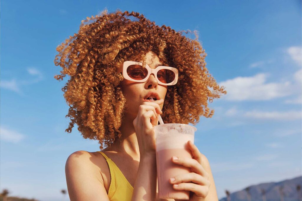 Femme aux cheveux bouclés savourant un smoothie au soleil